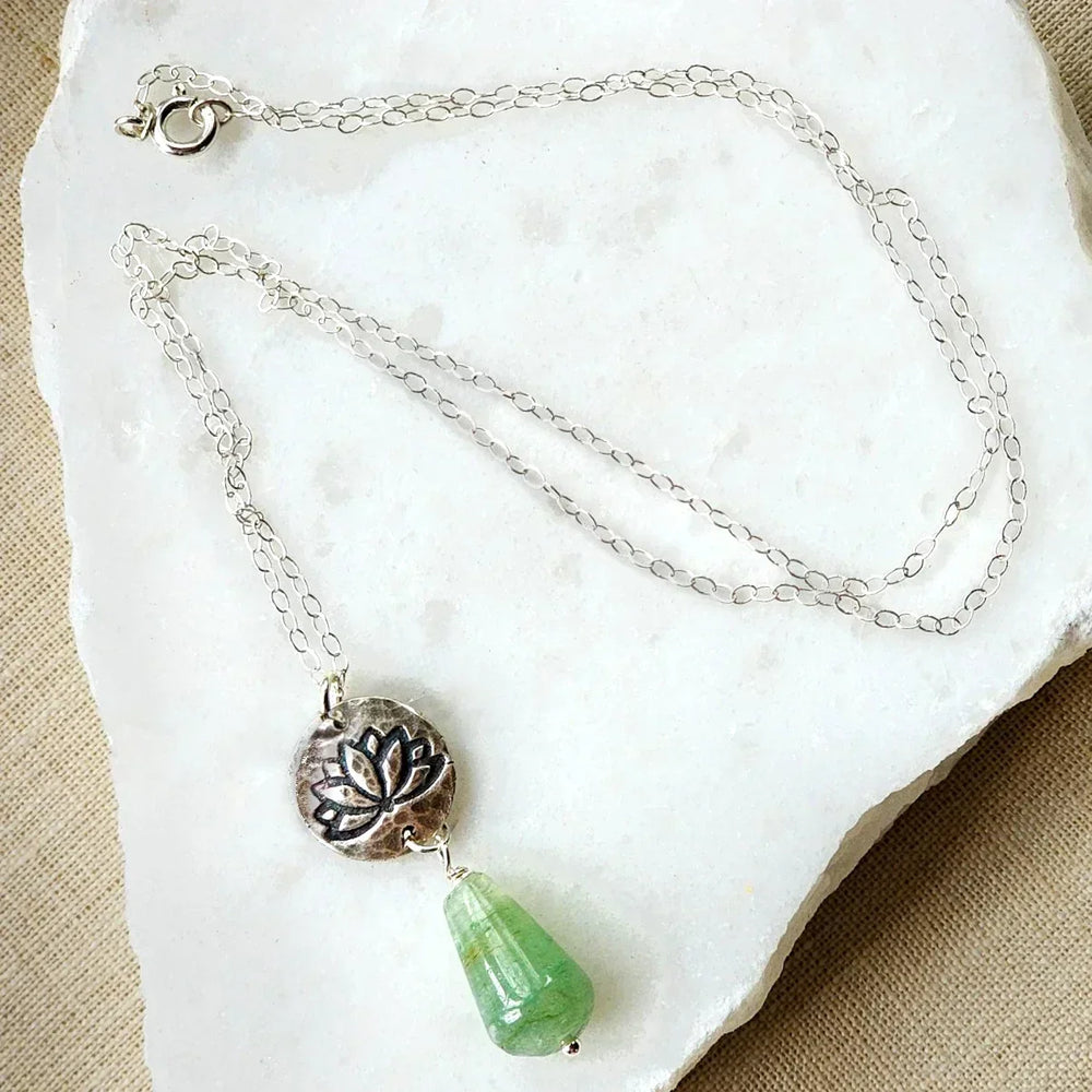 Green aventurine crystal and silver lotus disc necklace displayed on white stone background.