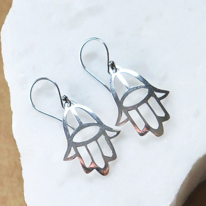 Pair of Silver Hamsa Hand Earrings on White Stone Background