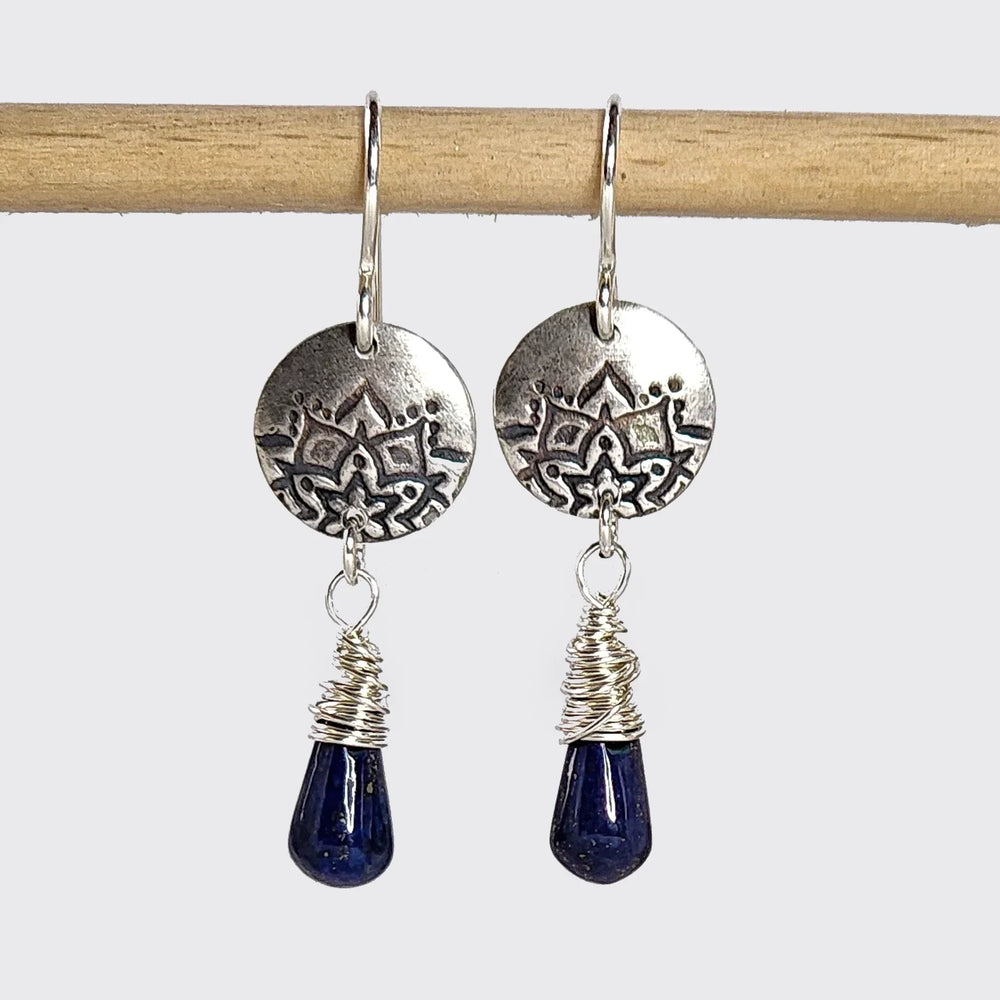 Silver lotus earrings with wire-wrapped lapis stones hanging from a wooden rod.