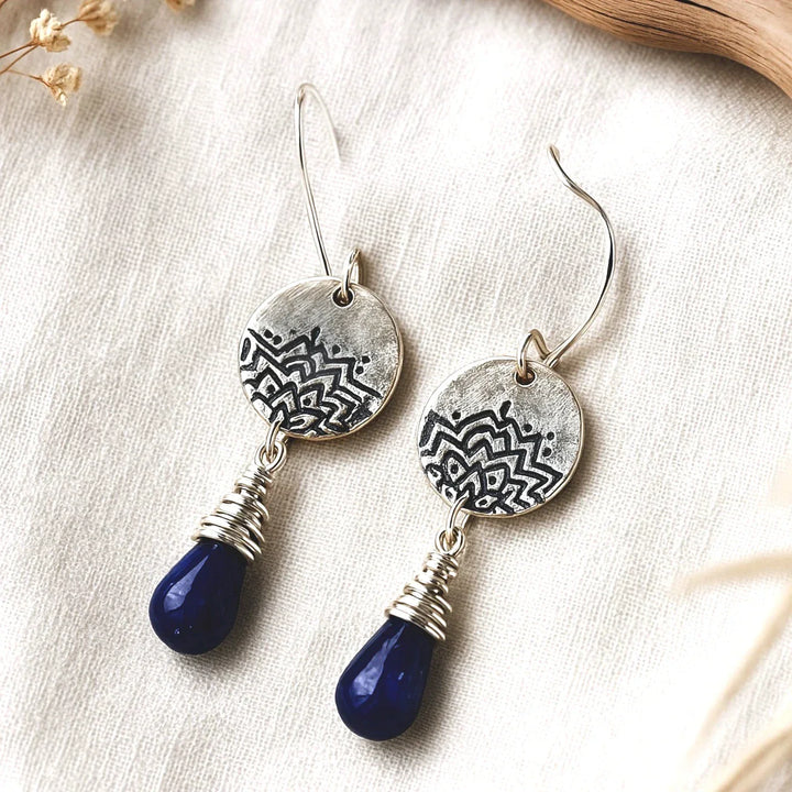 Photo of silver lotus earrings with lapis gemstone drops on linen fabric.