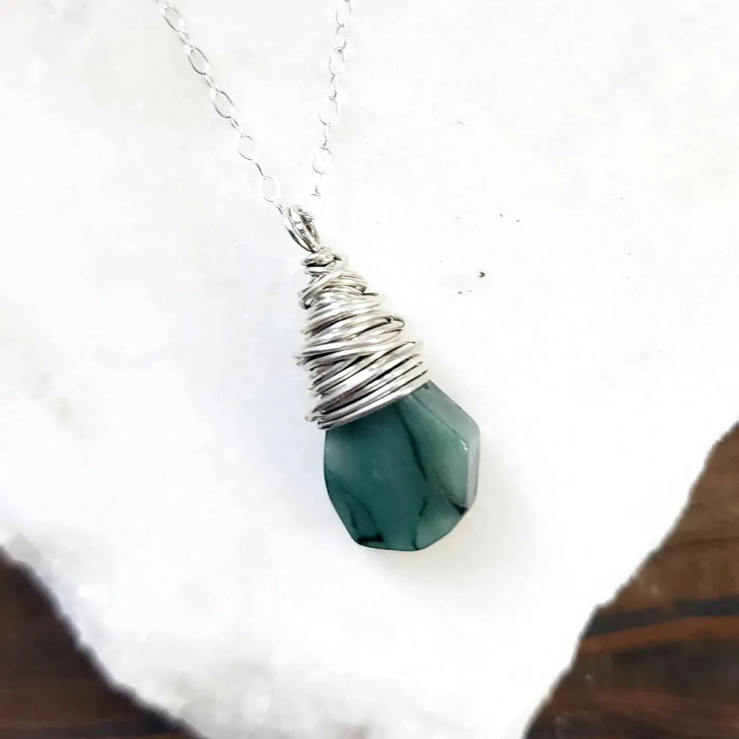 Sterling silver hand-wrapped gemstone necklace featuring a faceted emerald crystal wrapped in wire.