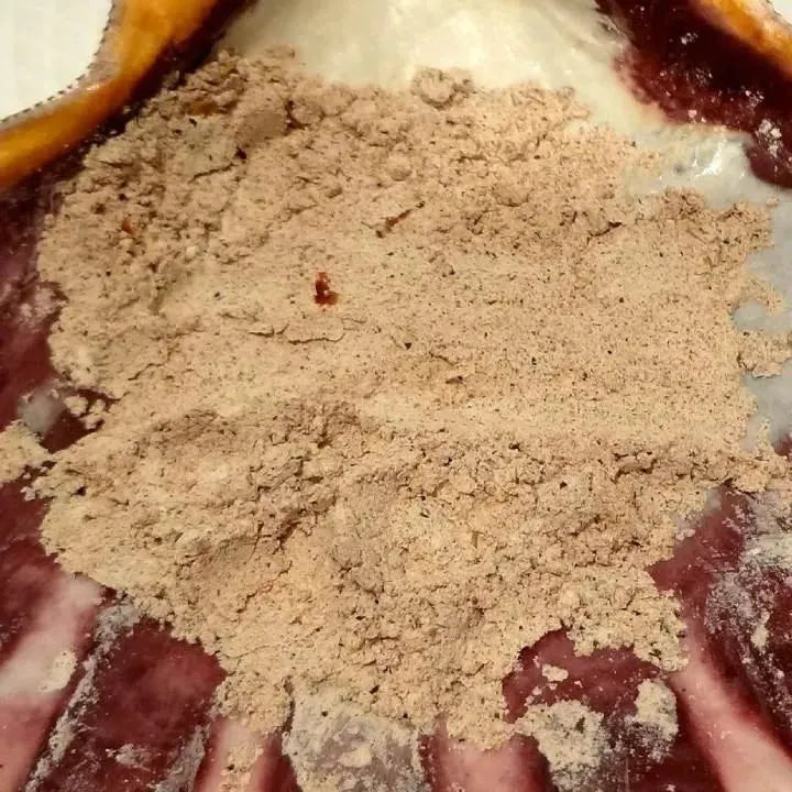 A pile of tan-colored Hot Foot Powder in a decorative shell with brown & cream tones.