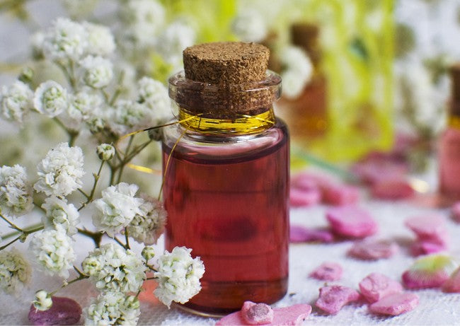 A Love and Attraction Magick Oil in a glass jar surrounded by flowers.