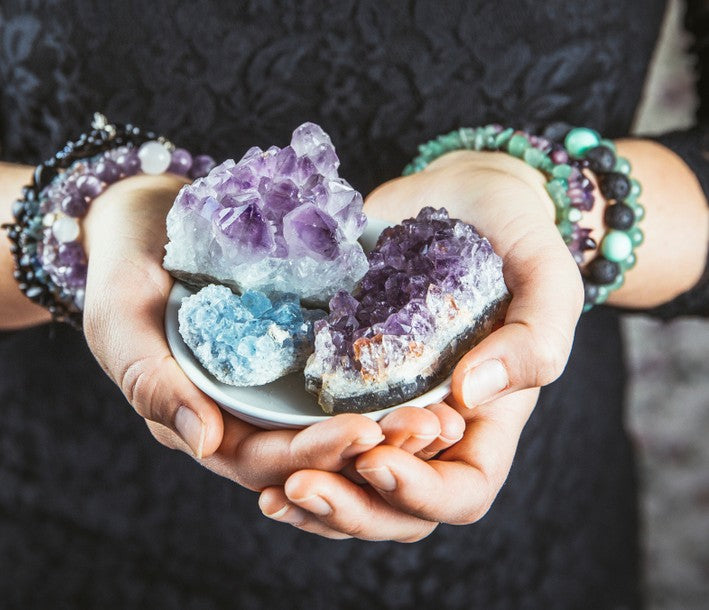 Someone holding unpolished amethyst and wearing crystal bracelets. Read Crystal Magic: Mastering Spells with Gemstones now.