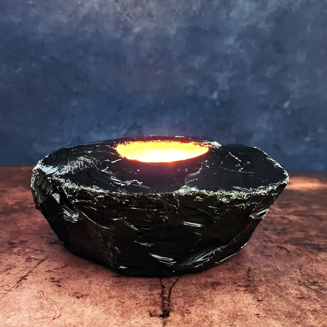 An Art of the Root Obsidian Crystal Candle Holder with a lit tea light candle inside.