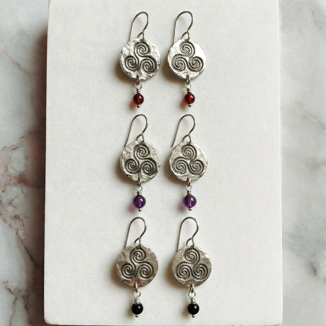 Triskele symbol silver earrings displayed on natural surface with gemstone drops