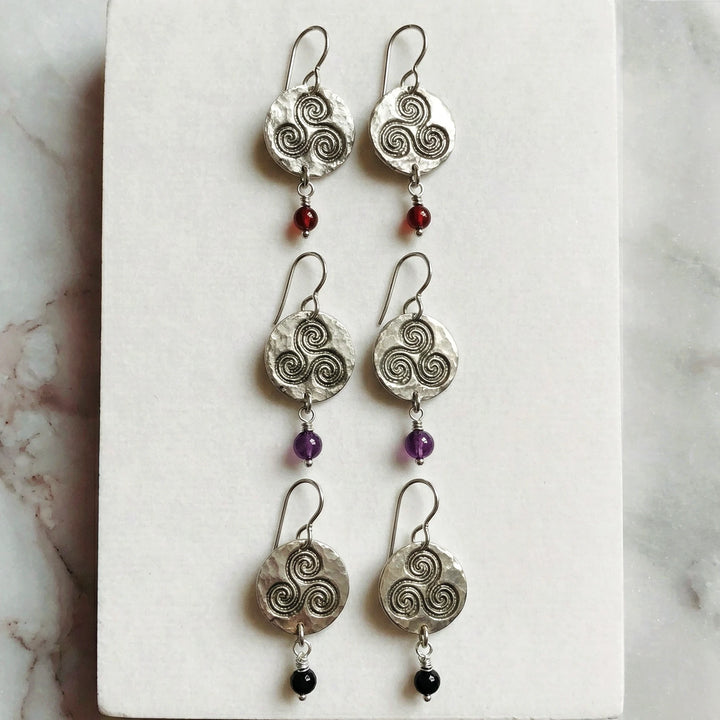 Triskele symbol silver earrings displayed on natural surface with gemstone drops
