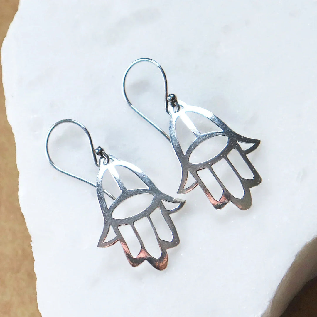 Pair of Silver Hamsa Hand Earrings on White Stone Background
