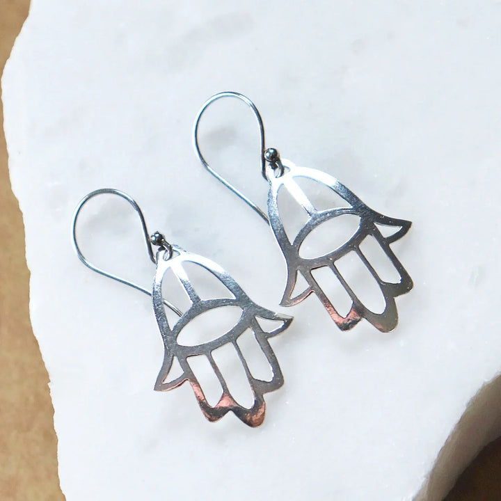 Pair of Silver Hamsa Hand Earrings on White Stone Background
