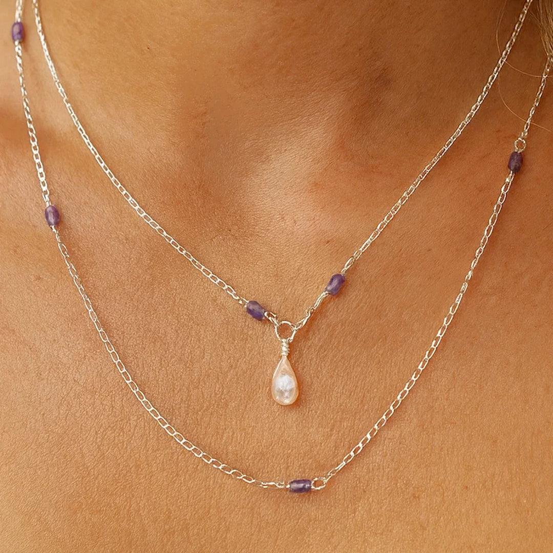 Sterling silver necklace with a teardrop flashy moonstone pendant and iolite beads on a person's neck.
