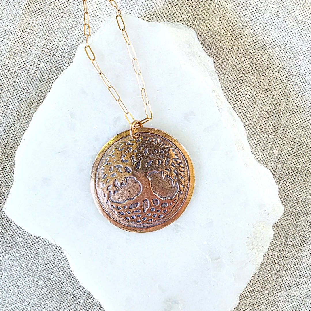 Bronze necklace with a circular pendant featuring an engraved design on a beige fabric background