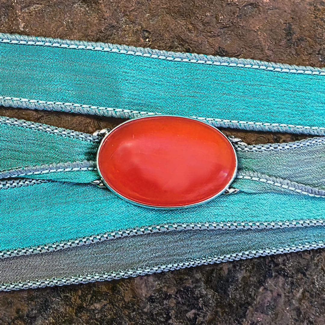 Gemstone Wrap Bracelet  with a carnelian stone and silver setting on a raw silk wrap on textured surface
